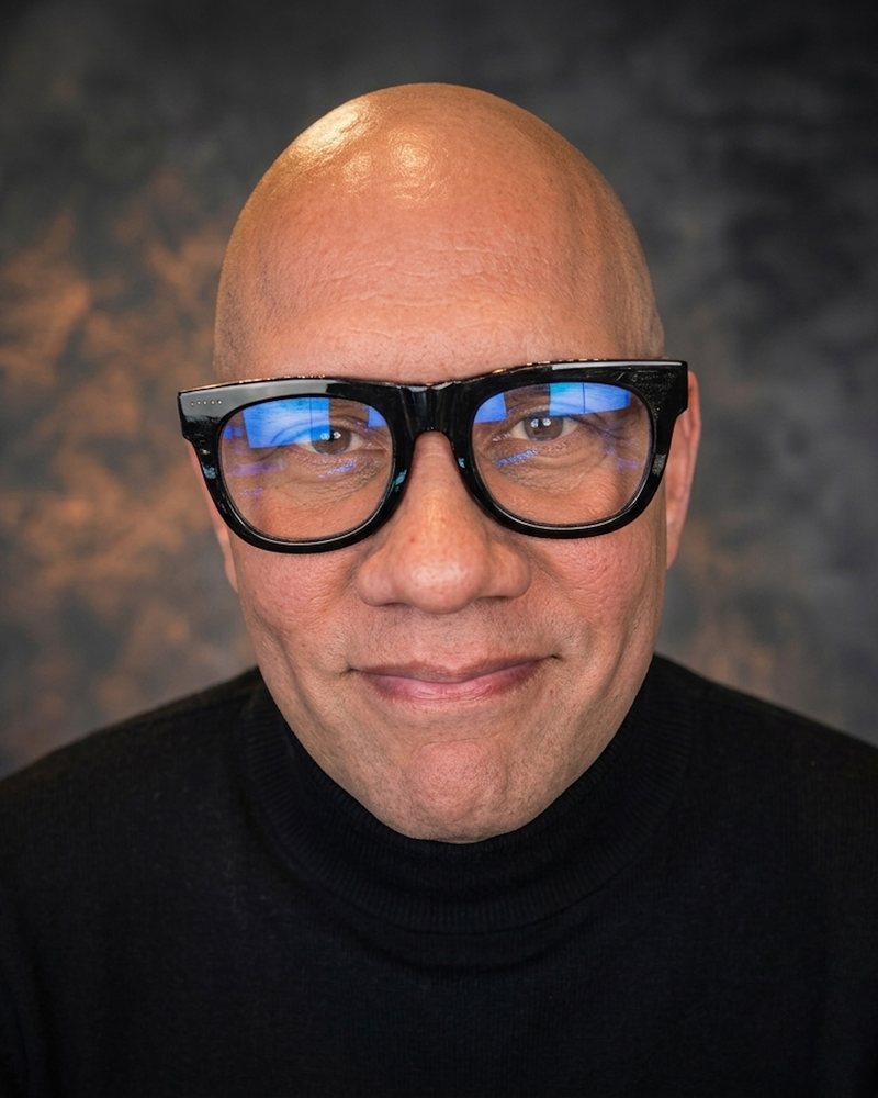 Harold Martinez, smiling, wearing thick black-framed glasses